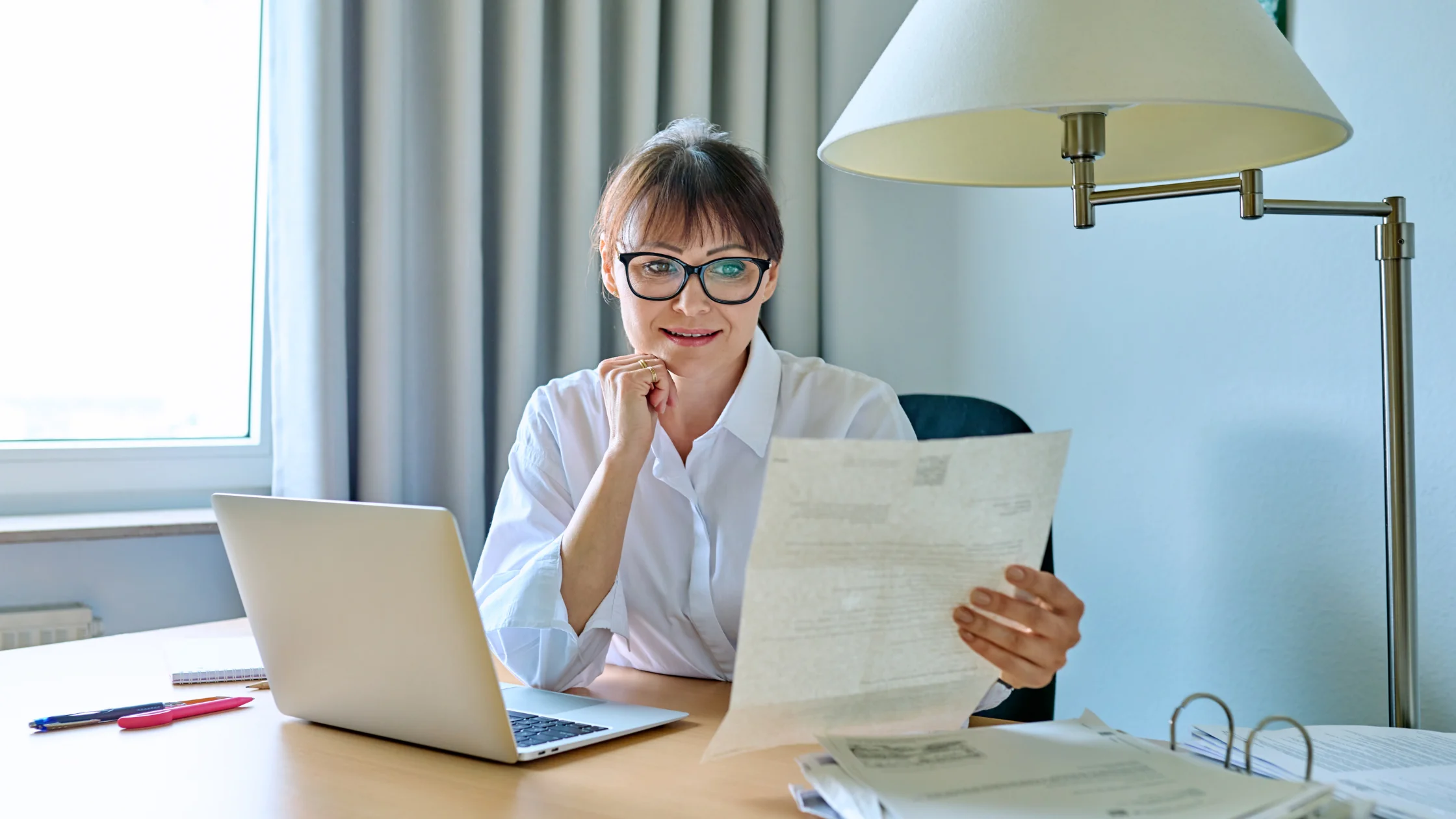 Frau mit Brille liest am Schreibtisch nachdenklich einen Brief zu ihrem Bildungsgutschein.