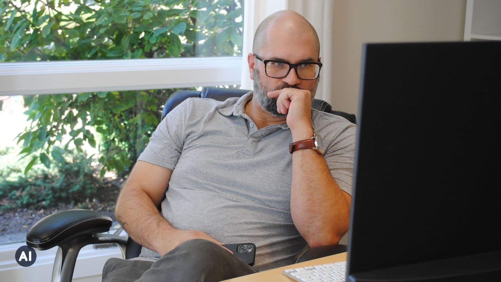 Mann sitzt nachdenklich mit der Hand am Kinn vor seinem Bildschirm im Büro (KI-generiert)