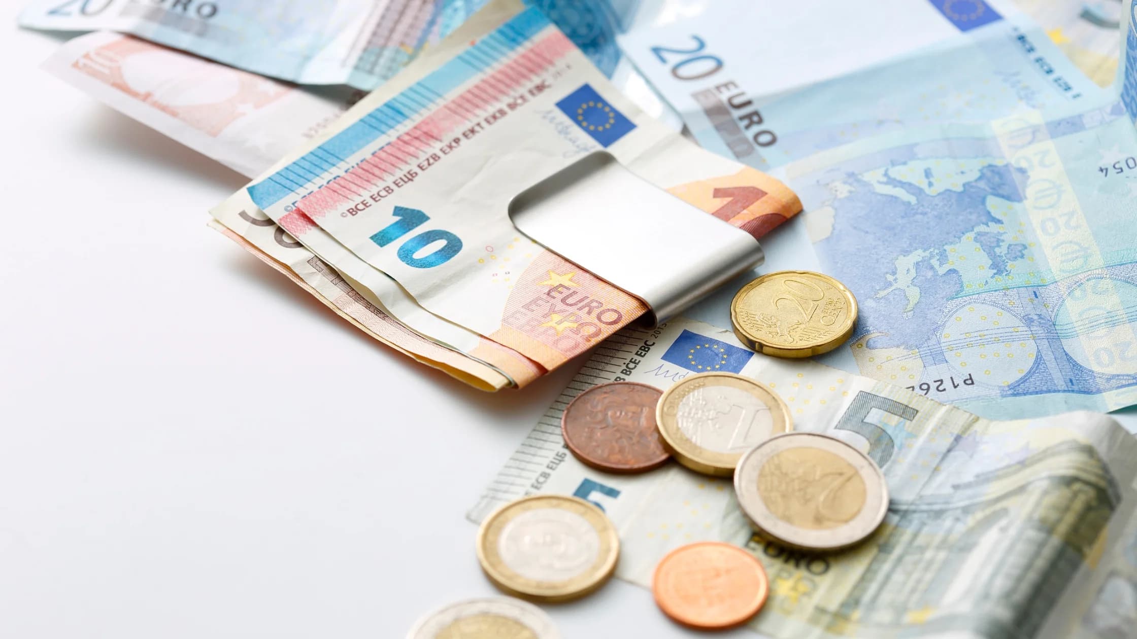 Euroscheine und Münzen liegen auf einer weißen Fläche, ein Teil der Scheine steckt in einer Geldklammer, als Sinnbild für die Höhe einer Abfindung.
