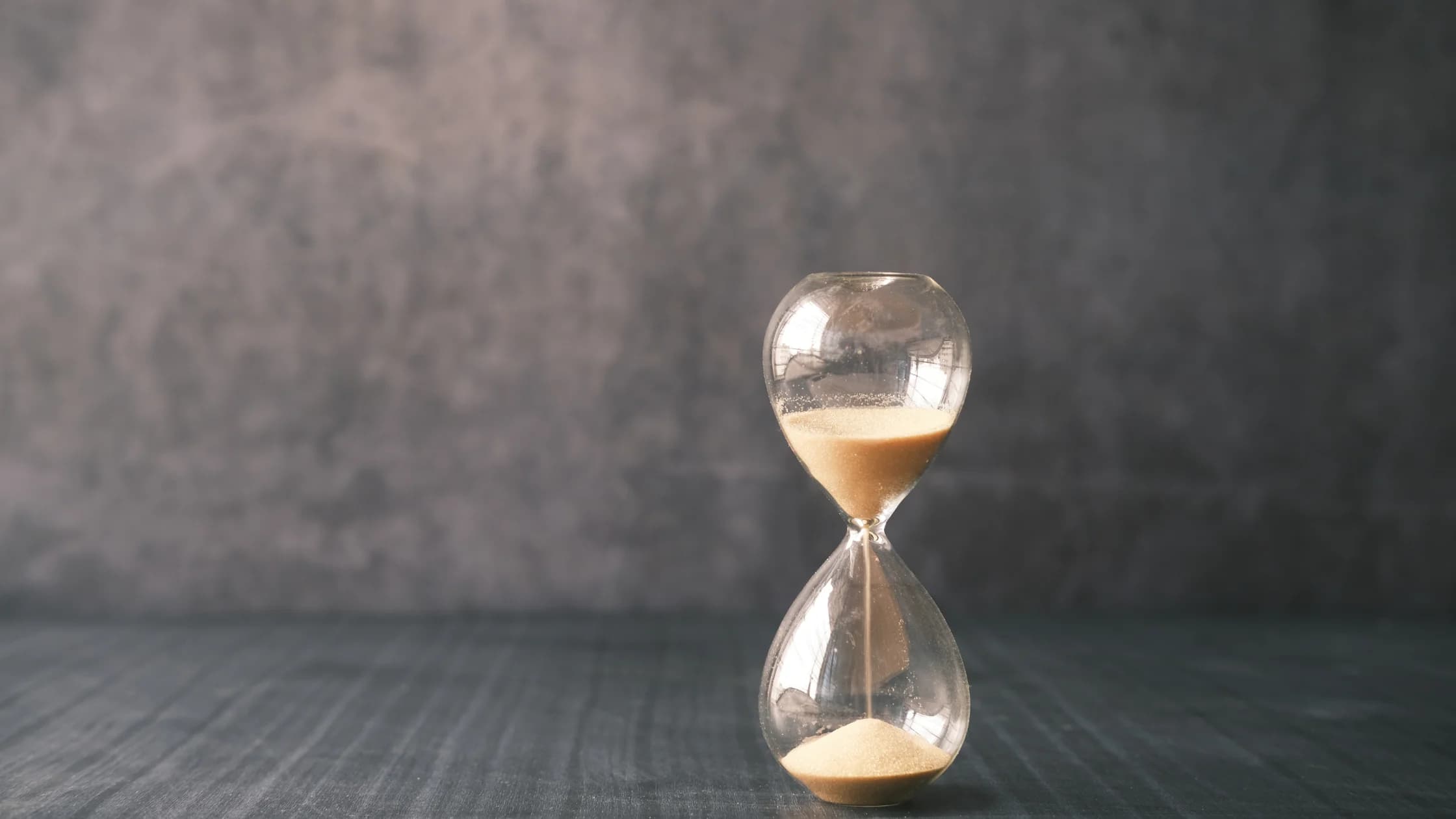 Eine Sanduhr steht auf einem Holztisch, als Sinnbild für die Zeit, in der das Arbeitslosengeld wegen einer Abfindung ruhen kann.