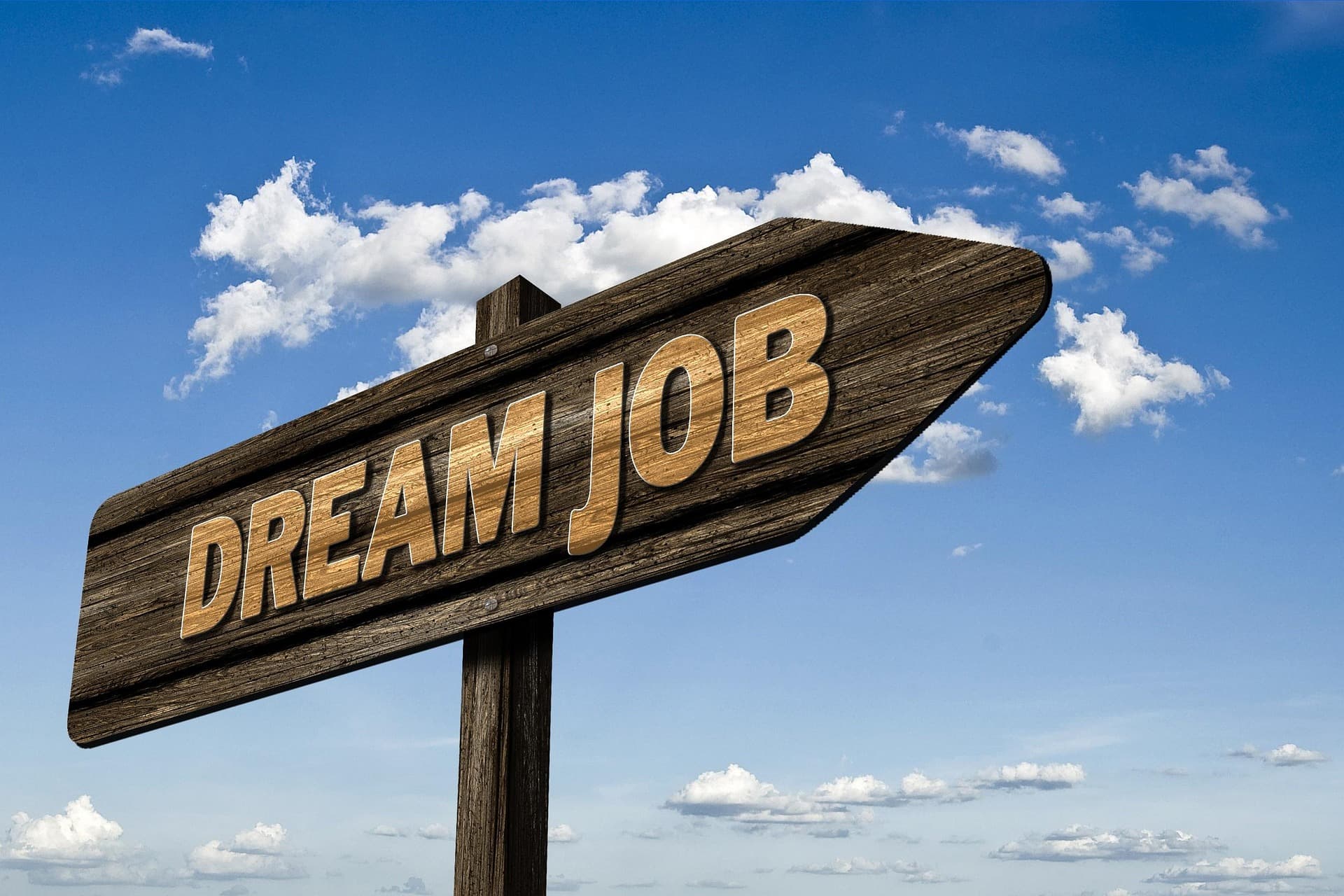 Hölzernes Wegweiser-Schild mit der Aufschrift „Dream Job“ vor blauem Himmel