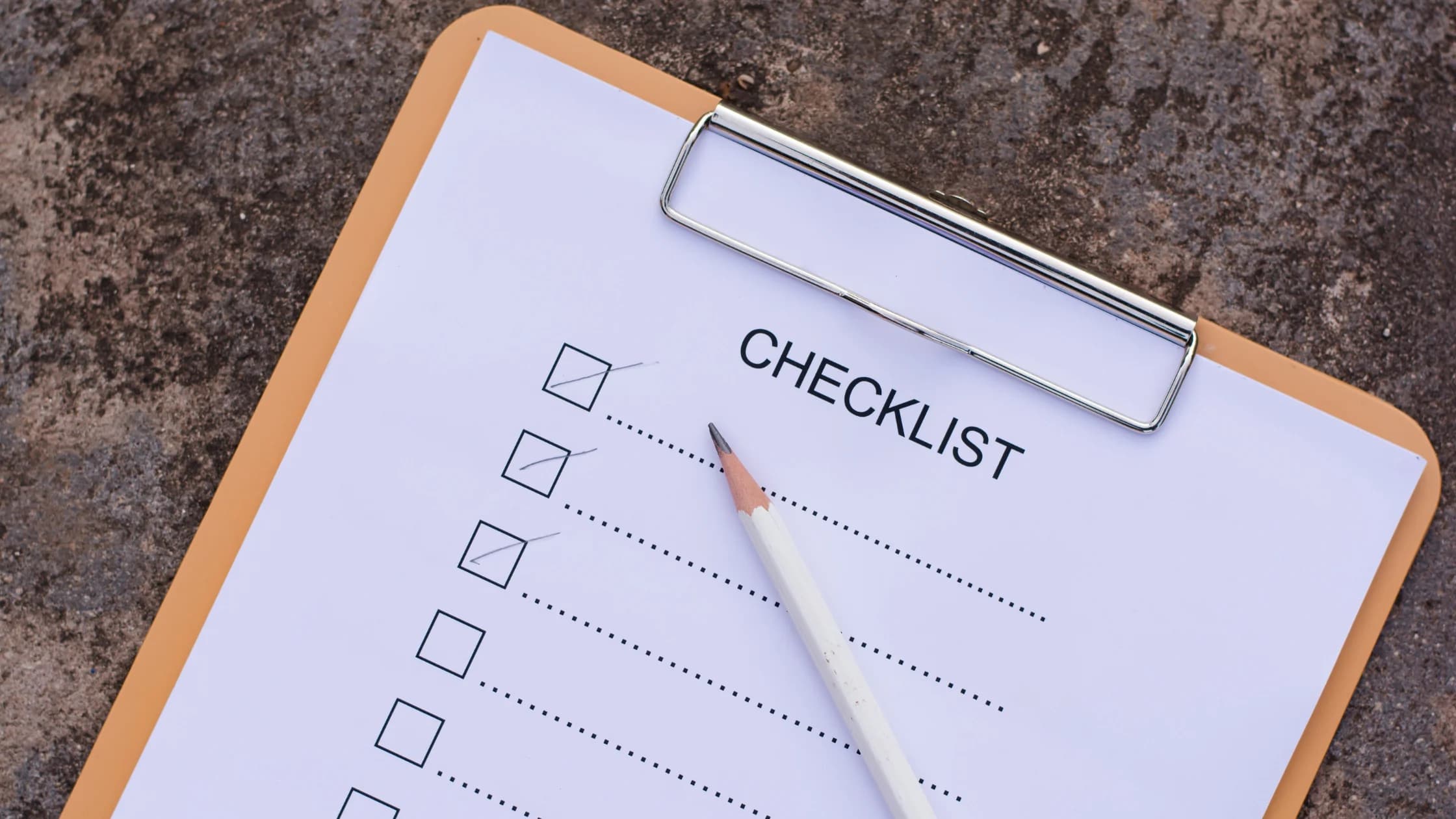 Klemmbrett mit einer Checkliste, drei Kästchen sind abgehakt, darauf liegt ein weißer Bleistift, als Sinnbild für die Vorbereitung auf das Beratungsgespräch