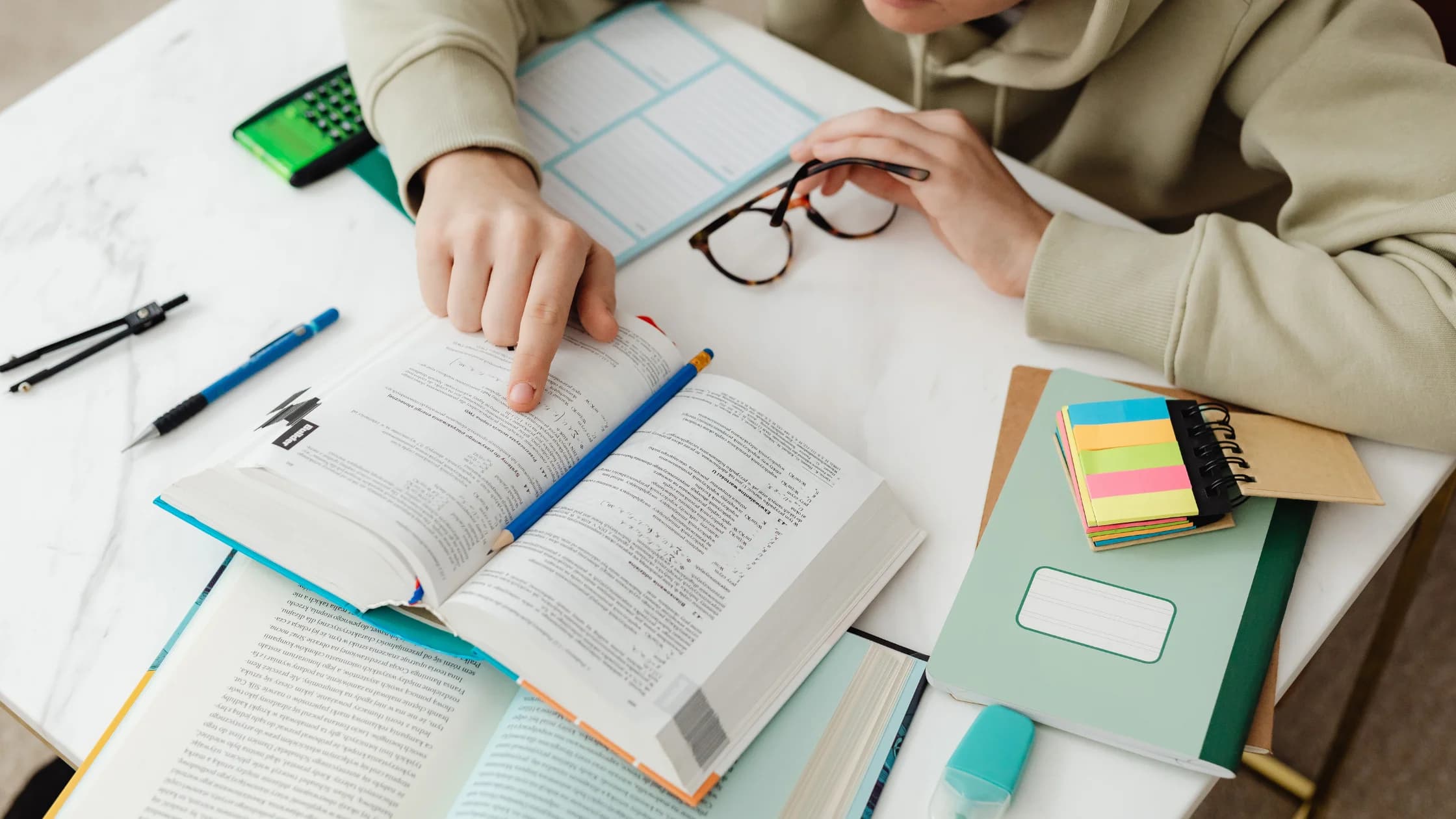 Person liest in einem aufgeschlagenen Fachbuch, daneben Notizblöcke, Stifte und Haftnotizen auf einem Tisch, als Symbol für die Vorbereitung auf eine geförderte Weiterbildung